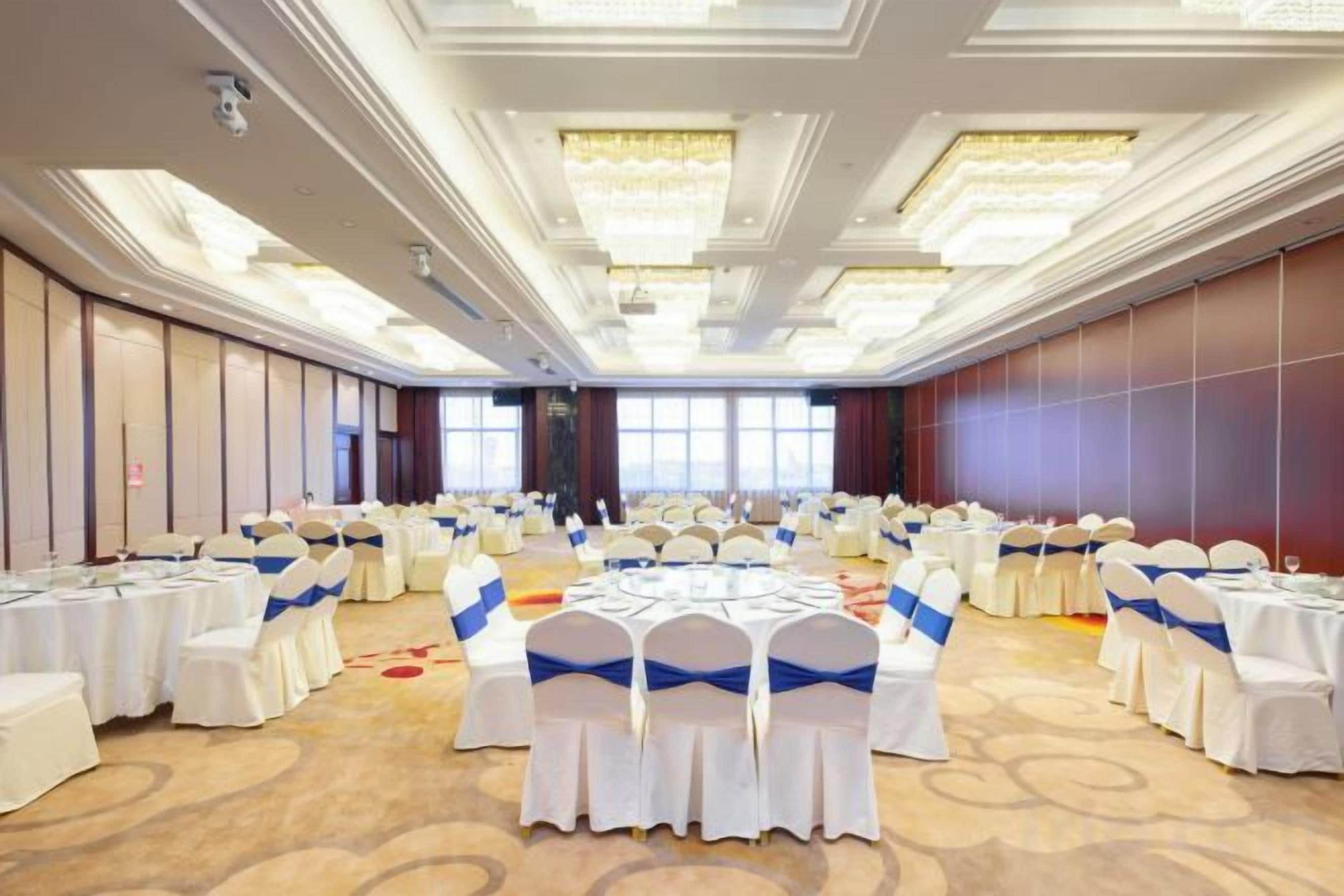 Un salón de banquetes con mesas redondas, manteles blancos y cintas azules.