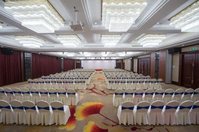 Un salón de conferencias con filas de sillas, un escenario y una alfombra con motivos florales.