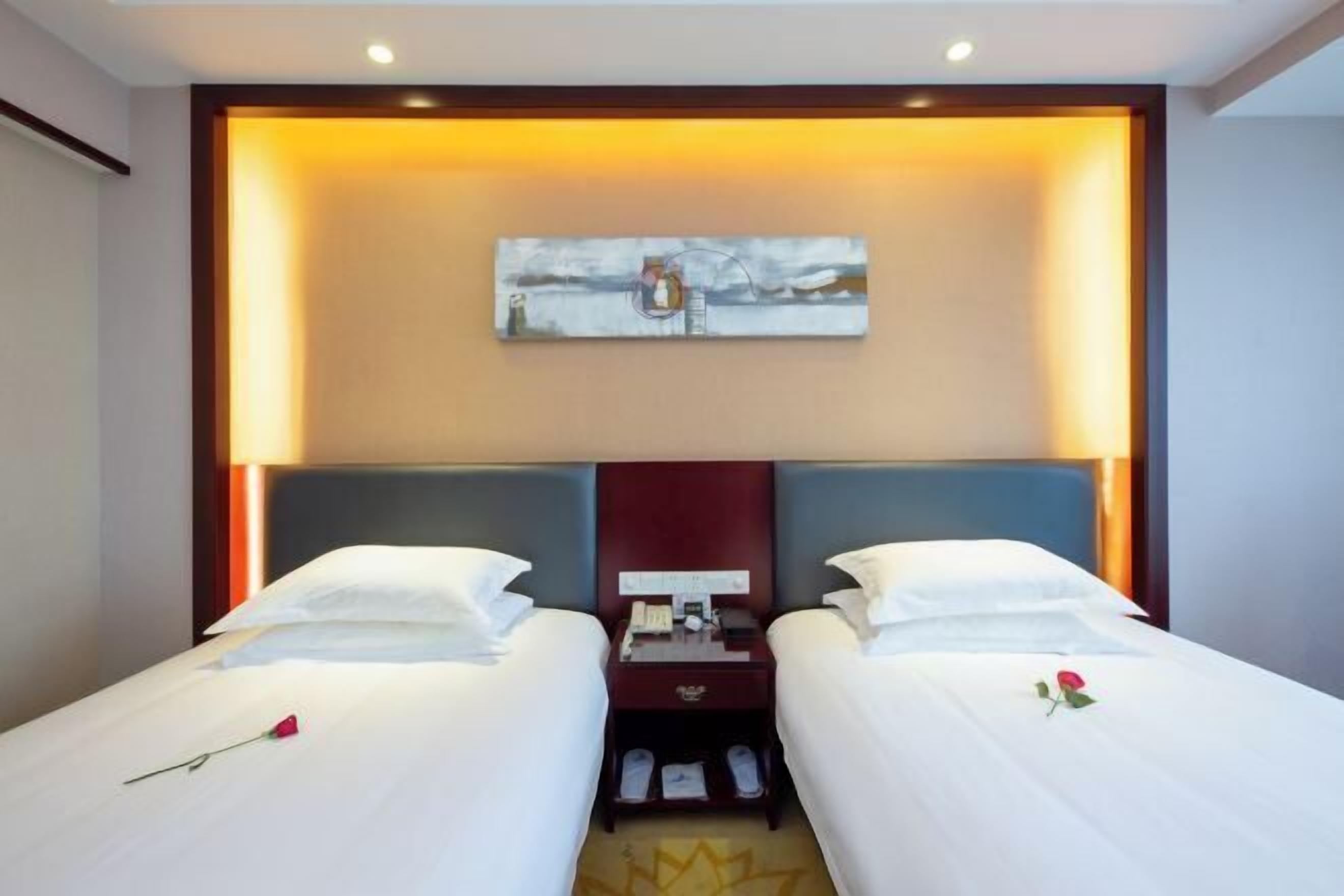 Hotelkamer met twee bedden, een nachtkastje, een schilderij aan de muur en een roos op de bedden.