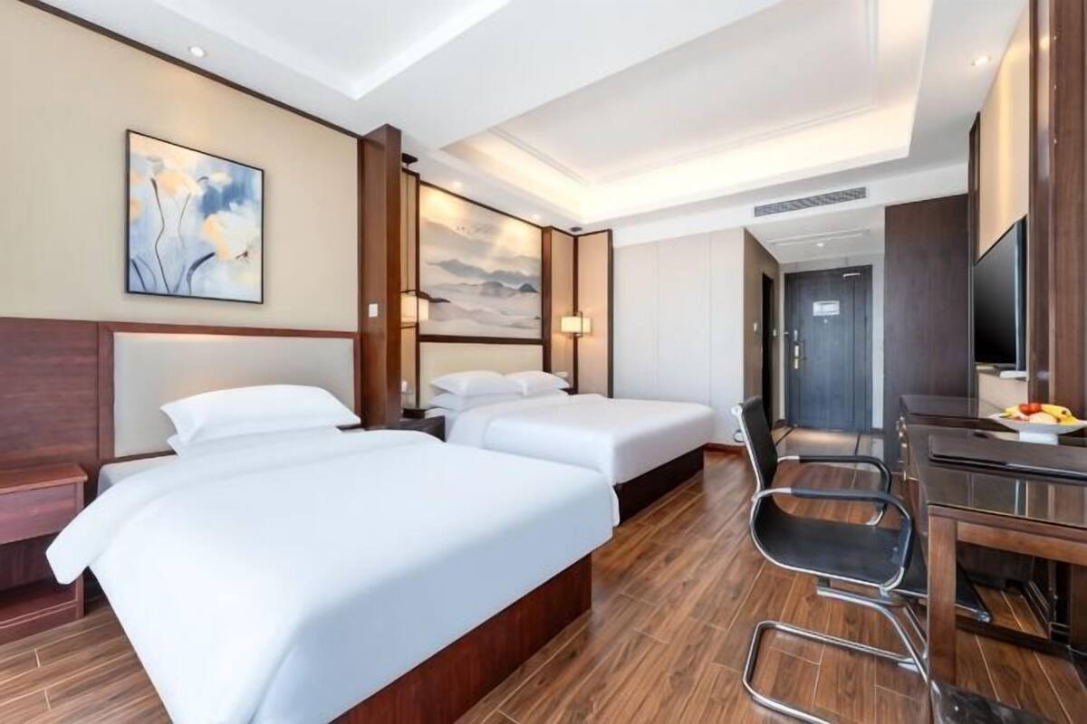 Une chambre d’hôtel avec deux lits, un bureau avec une chaise, une télévision et des œuvres d’art accrochées aux murs.