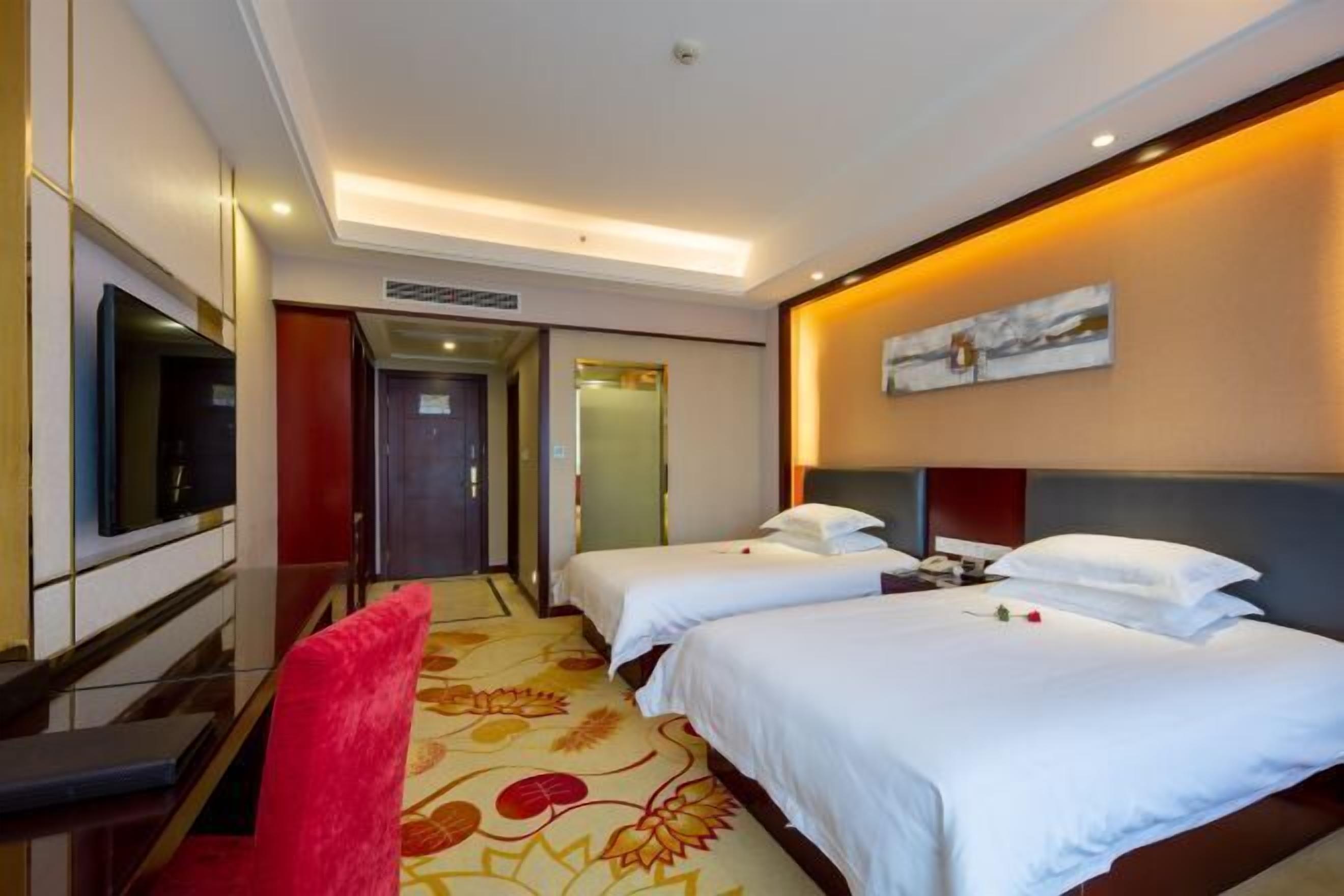 Een hotelkamer met twee bedden, een televisie, een bureau en een rode stoel.