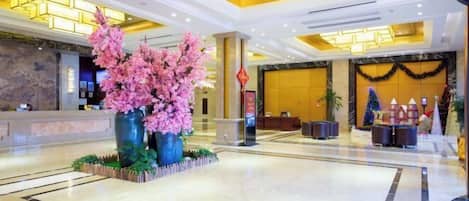 A lobby with a reception desk, a large artificial pink tree, and a Christmas tree.