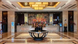 Un vestíbulo de hotel con mostrador de recepción, un arreglo floral grande y un candelabro moderno.