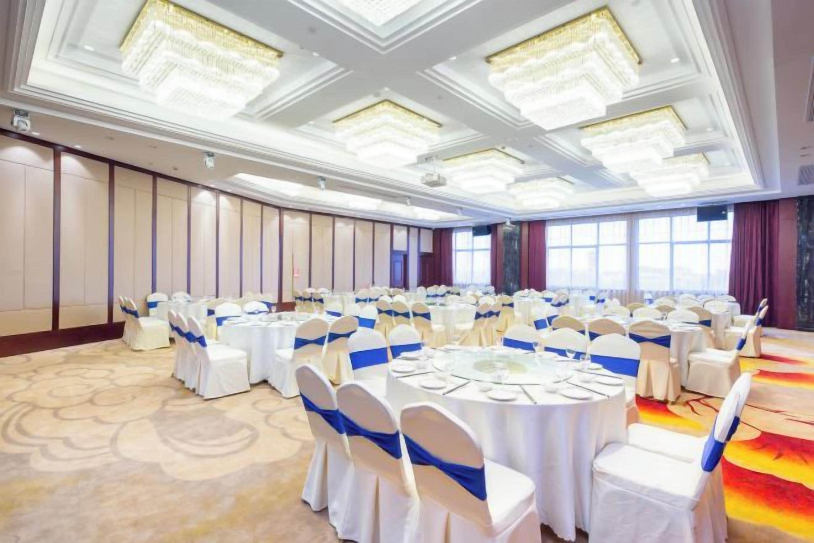 Un salón de banquetes con mesas redondas, manteles blancos y cintas azules.