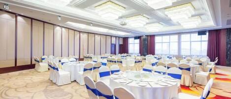 Un salón de banquetes con mesas redondas, manteles blancos y cintas azules.