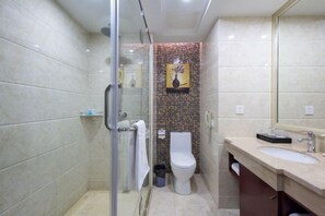 Een moderne badkamer met een douchecabine van glas, een wit toilet en een beige wastafelmeubel met spiegel.