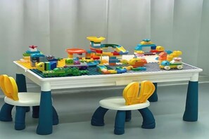 Une table surmontée d’une maquette de paysage urbain en LEGO et quatre chaises aux accents jaunes et bleus.