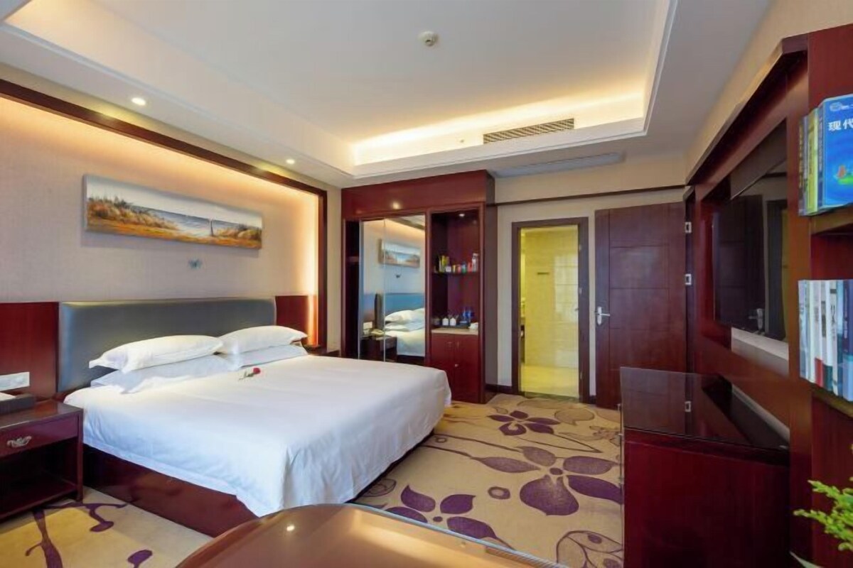 Une chambre d’hôtel avec un grand lit, un bureau, une armoire et un téléviseur.