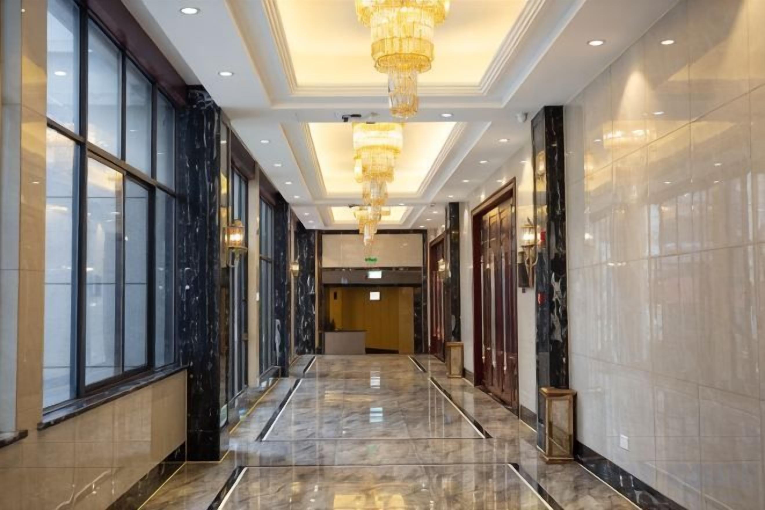A hotel corridor with marble flooring, large windows, and a chandelier.