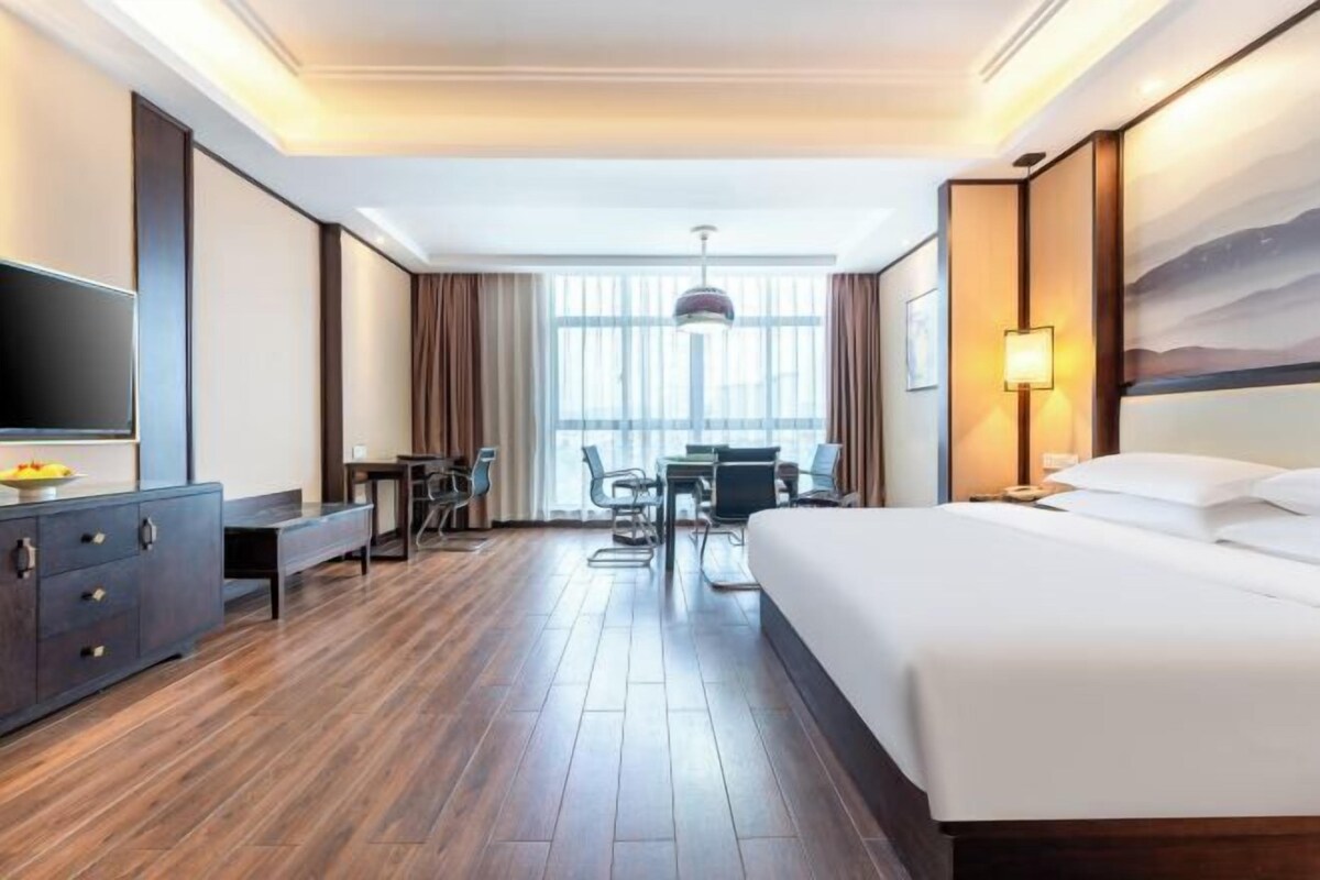 Une chambre d’hôtel dotée d’un grand lit, d’un bureau avec une chaise, d’une télévision et d’un coin repas avec une table et des chaises.