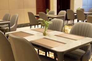 Une salle de conférence avec des tables et des chaises, une plante servant de décoration centrale et un mur recouvert de carreaux.