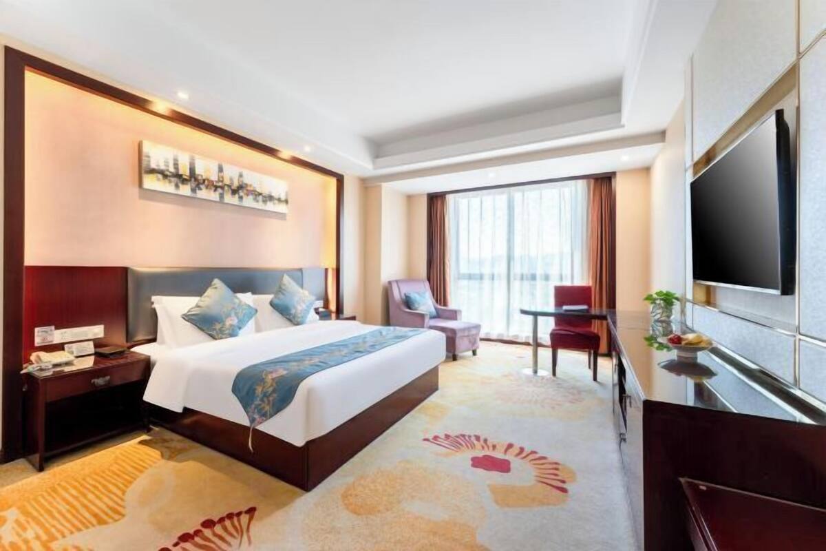 Une chambre d’hôtel avec un grand lit, un bureau doté d’un téléviseur à écran plat, une chaise et une fenêtre avec des rideaux.