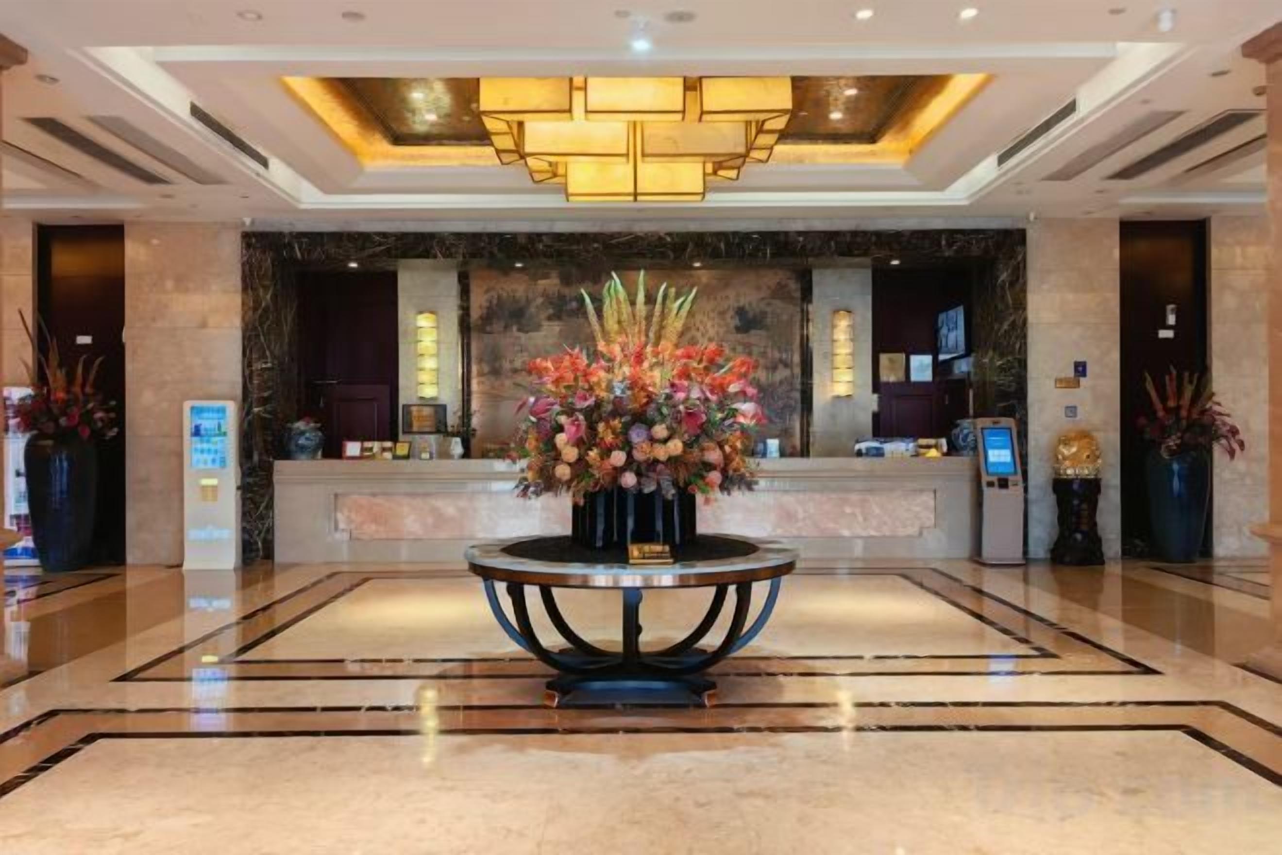 A hotel lobby with a reception desk, a large floral centerpiece, and a modern chandelier.