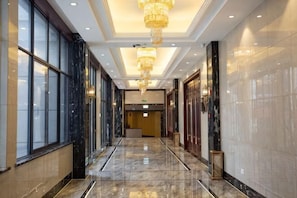 A hallway with marble floors, large windows, and a chandelier.