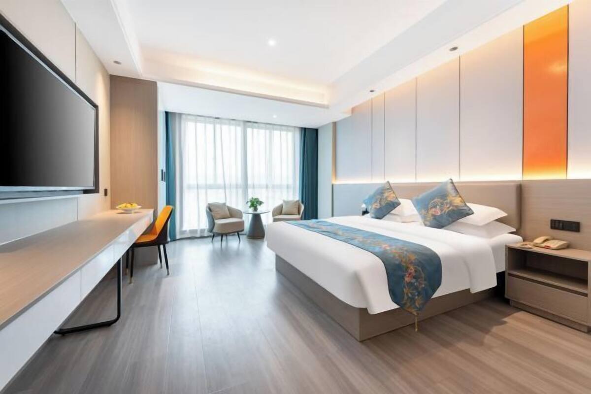 Une chambre d’hôtel moderne dotée d’un grand lit, d’un bureau, d’une télévision et d’un coin salon avec des fauteuils.
