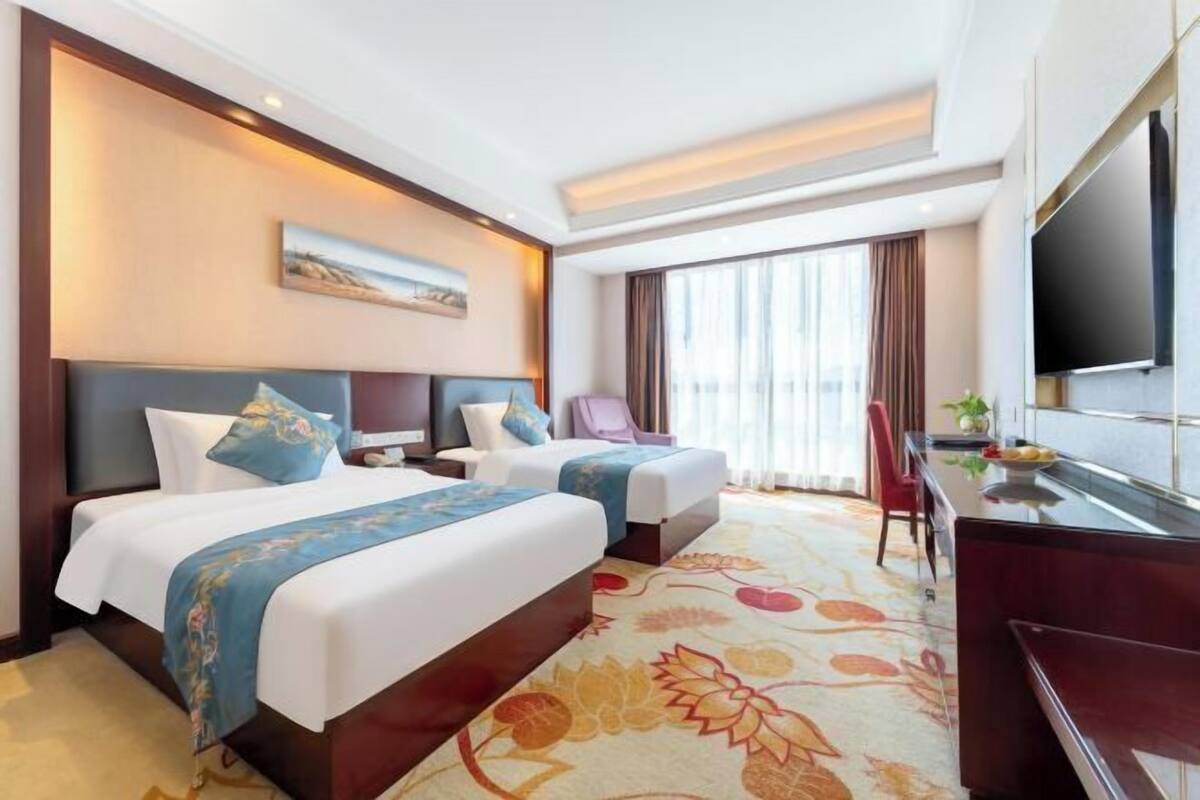 Une chambre d’hôtel avec deux lits, un bureau, une télévision et une grande fenêtre.