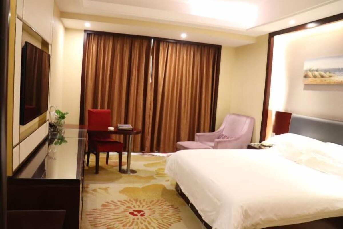 Une chambre d’hôtel avec un lit, un bureau, une chaise, une télévision et un rideau.