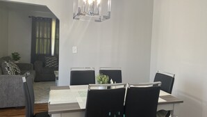 Ein Essbereich mit einem Tisch, der für vier Personen gedeckt ist, umgeben von Stühlen. Über dem Tisch hängt ein moderner Kronleuchter.