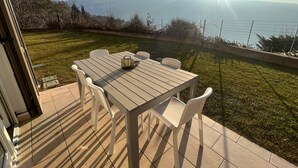 Une terrasse avec une table et des chaises, donnant sur une pelouse et des montagnes.