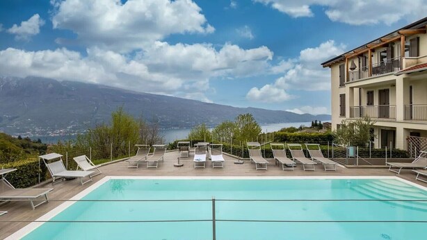 Une piscine avec des chaises longues, une vue sur les montagnes et un bâtiment doté de balcons.