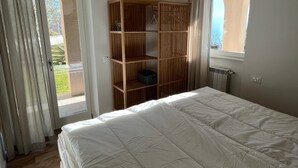Une chambre avec un grand lit, une armoire en bois, un luminaire suspendu et une vue par la fenêtre.