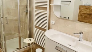 Une salle de bain moderne avec une douche à parois de verre, un lavabo blanc, un porte-serviettes et un miroir agrémenté d’un élément décoratif en bois.