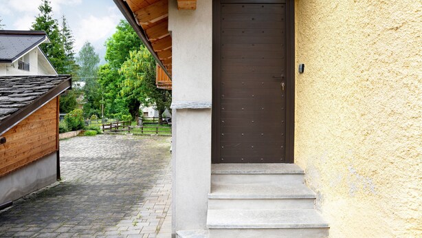 A building with a stone staircase leading to a dark wooden door, a cobblestone path, and a wooden fence in the background.