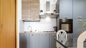 A modern kitchen with grey cabinets, a stainless steel range hood, a built-in oven, and a dining area with a white chair. - Apartment "Casa Lucy" with Lake View, Shared Pool & Wi-Fi (Tremosine sul Garda)
