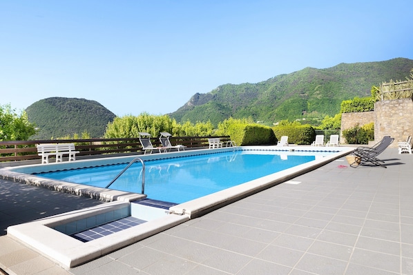 Piscina com vista para montanhas, cadeiras de descanso e um muro de pedra.