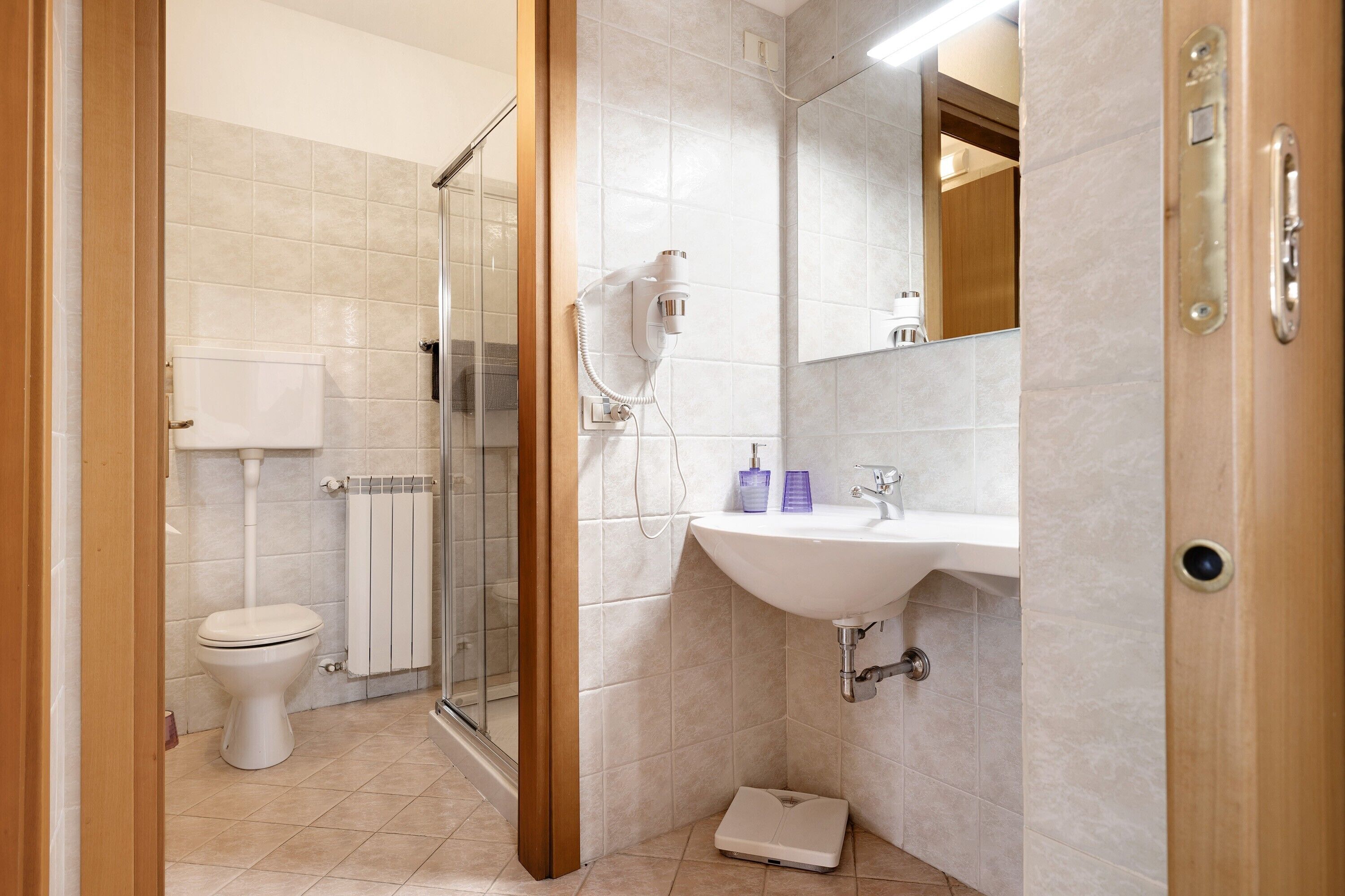 Un baño con inodoro, ducha, lavamanos y una balanza.