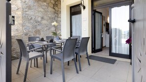 A dining area with a stone wall, a table with chairs, a potted plant, and a view through a glass door. - Apartment "Casa Lucy" with Lake View, Shared Pool & Wi-Fi (Tremosine sul Garda)