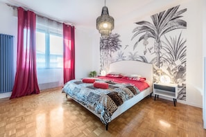 Une chambre à coucher avec une couvre-lit à motifs, un luminaire suspendu, une fresque murale et une table de chevet.