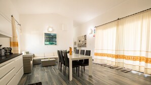 A modern kitchen with a dining area, a sofa, and a large window with curtains. - Holiday Home 'Villa S'ena E Su Juncu' with Mountain View, Wi-Fi & Air Conditioning (loculi)