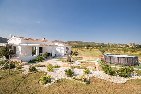 A white building with a tiled roof, a swimming pool, and a garden with rocks and plants.