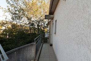 A narrow corridor with a metal railing, a tiled floor, and a white wall.