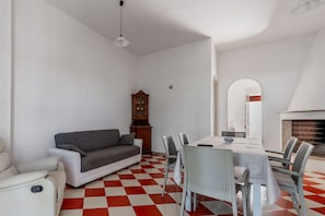 A living room with a sofa, dining table, chairs, a fireplace, and a checkered floor.