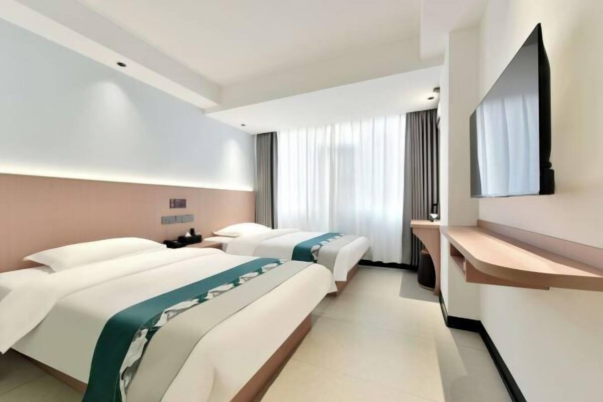 A hotel room with two beds, a flat-screen TV, a bedside table, and a large window with curtains.