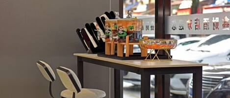 Une table avec un bol, des baguettes et une petite figurine. Il y a deux chaises et une fenêtre donnant sur des voitures garées.