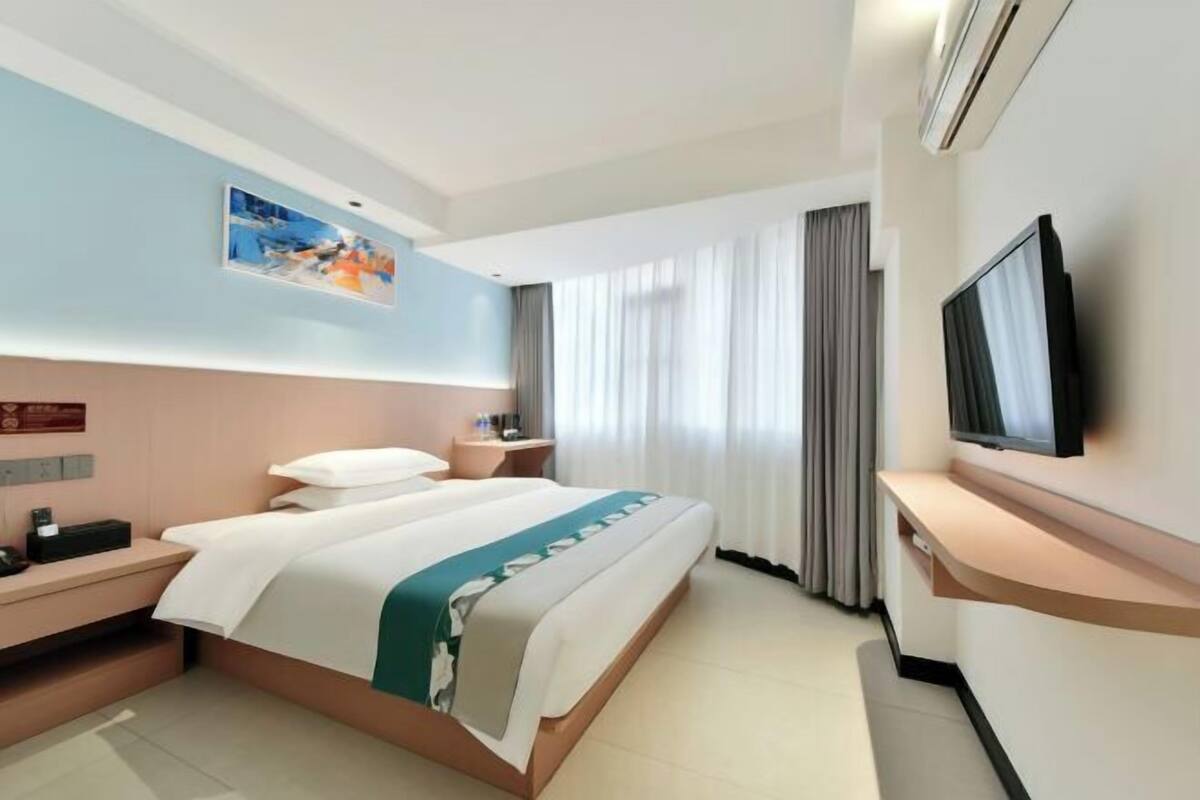 A hotel room with a bed, a TV, a desk, a nightstand, and a window with curtains.
