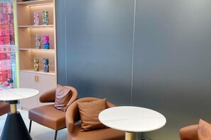 A modern interior with a sofa and two round tables, a shelf with decorative items, and a grey wall. - Xincai Hotel (Nanning Chaoyang Square Railway Station Subway Station Store) (Nanning)