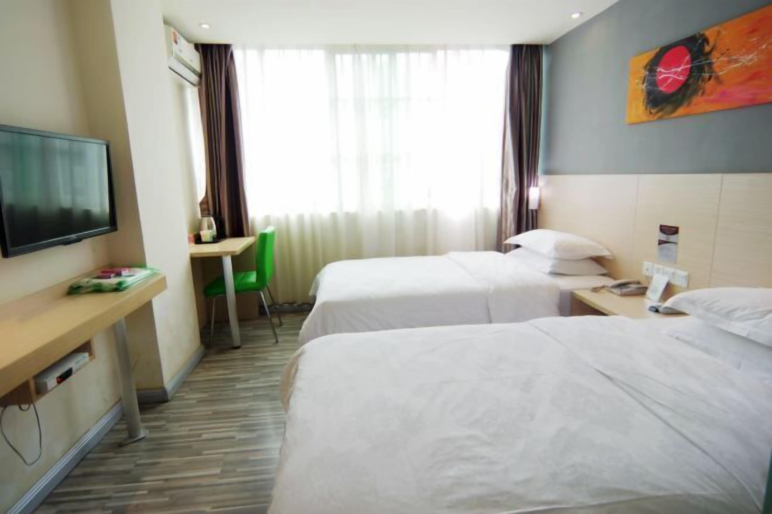 A hotel room with two beds, a desk, a chair, a television, and a painting on the wall.