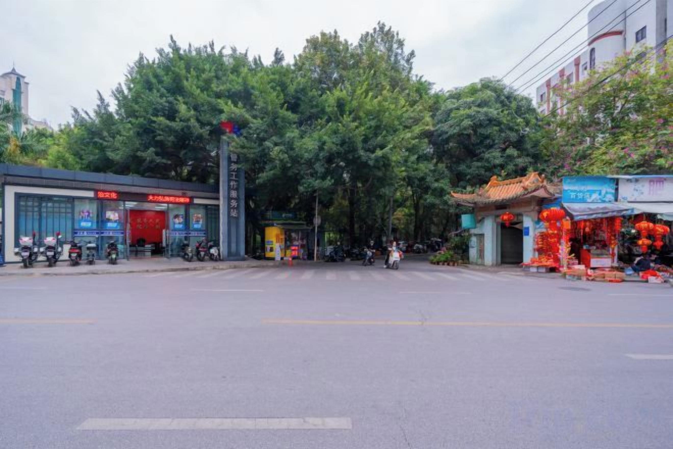 A street view with a building entrance, trees, and a shop with red decorations.