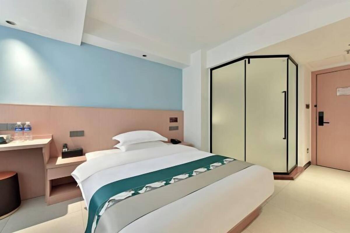 A hotel room with a bed, a desk, a wardrobe, and a shower area.