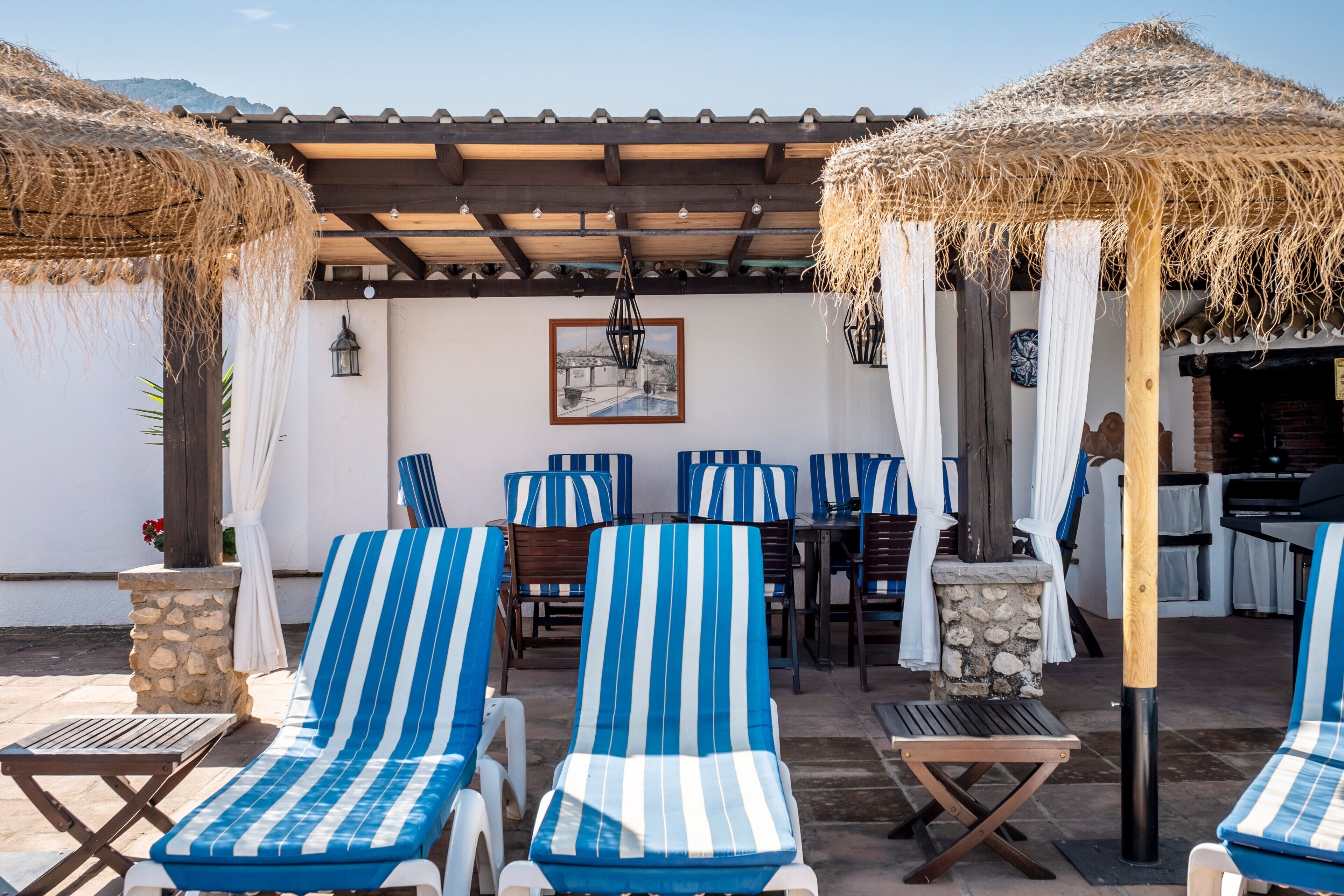 A patio with striped lounge chairs, a stone pillar, and a thatched umbrella.