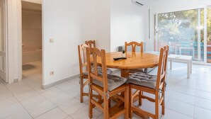 A dining area with a round wooden table and six chairs, a potted plant, and a remote control on the table. - Aiguablava Apartments 1 (Begur)
