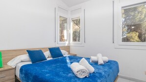A bedroom with a bed, pillows, a nightstand, and two windows. - Aiguablava Apartments 1 (Begur)