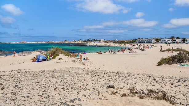 Platja amb gent, tendes i edificis al fons.