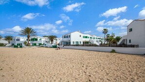 Una platja sorrenca amb edificis blancs, palmeres i un cel blau clar.