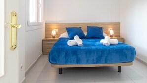 A neatly made bed with blue bedding and white towels, a wooden headboard, and bedside lamps. - Aiguablava Apartments 3 (Begur)