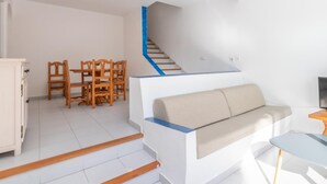 A modern living room with a staircase, a sofa, a dining table with chairs, and a TV. - Aiguablava Apartments 3 (Begur)